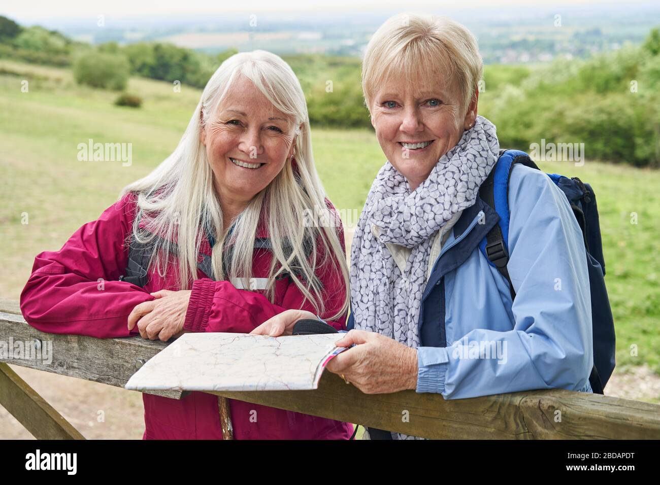 Portrait Of Two Retired Senior Friends On Walking Holiday Resting On Gate Looking At Map Stock Photo