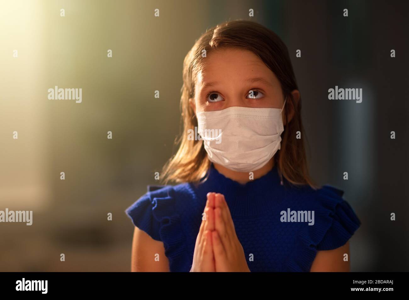 Pray for the sick. Child in face mask praying. Little girl in hospital chapel or church during coronavirus outbreak. Virus pandemic. Kids worship. Chi Stock Photo