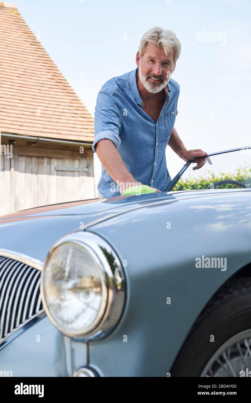 Portrait Of Mature Man Polishing Restored Classic Sports Car Outdoors At Home Stock Photo