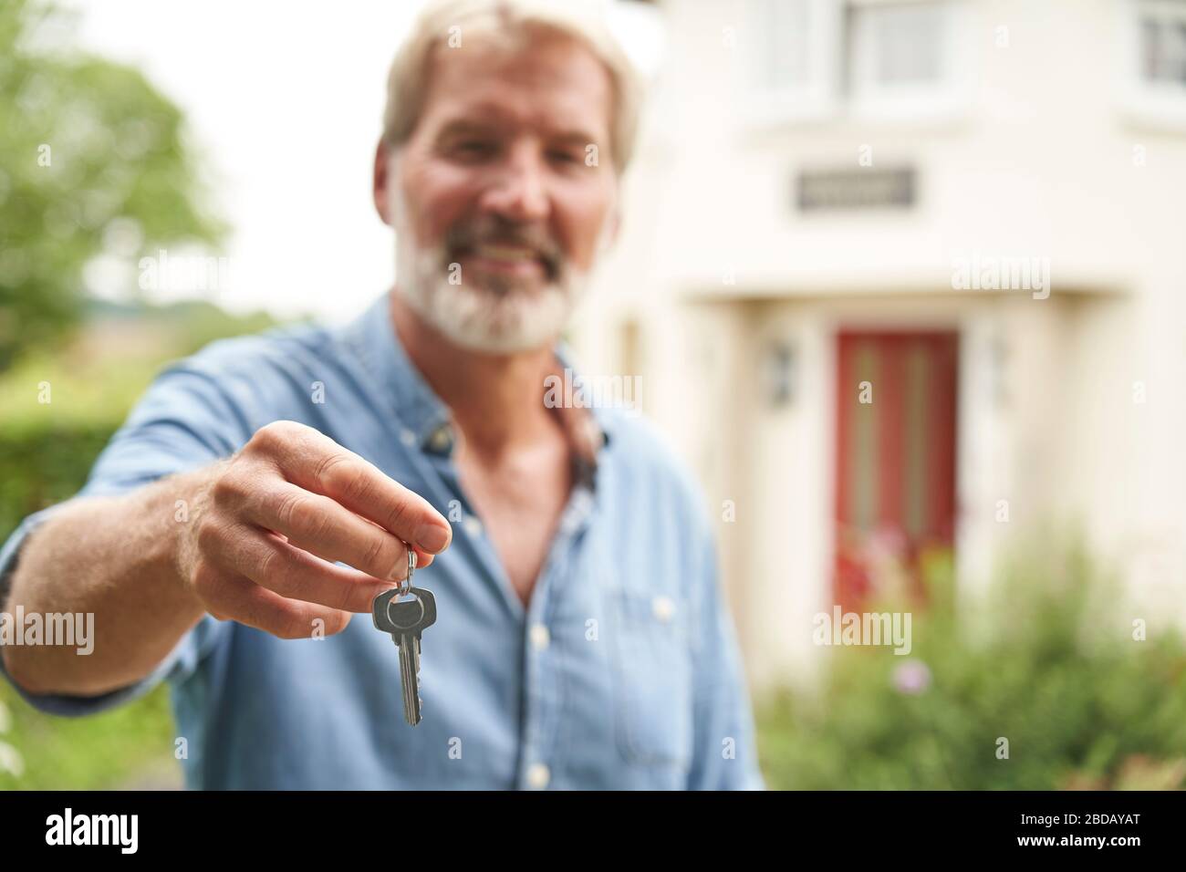 Portrait Of Mature Man Standing In Garden In Front Of Dream Home In Countryside Holding Keys Stock Photo