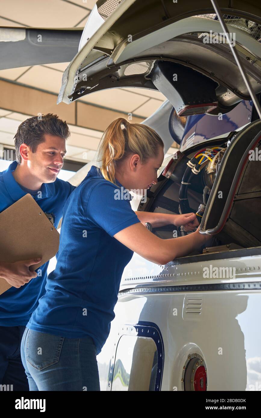 Aero Engineer And Apprentice Working On Helicopter In Hangar Stock Photo