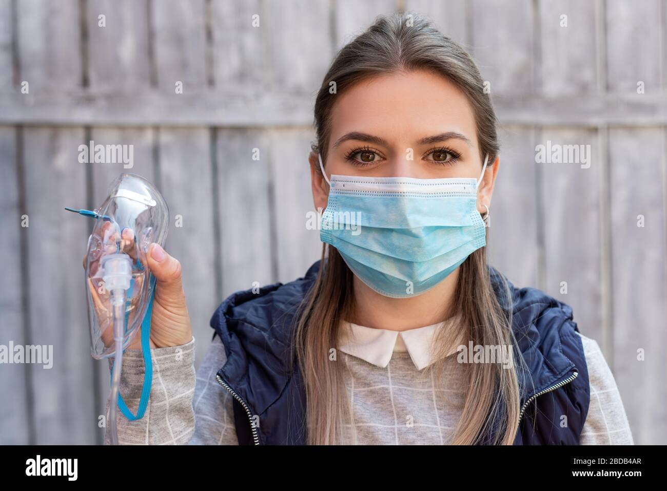 Woman wearing surgical mask is holding a medical oxygen mask outside