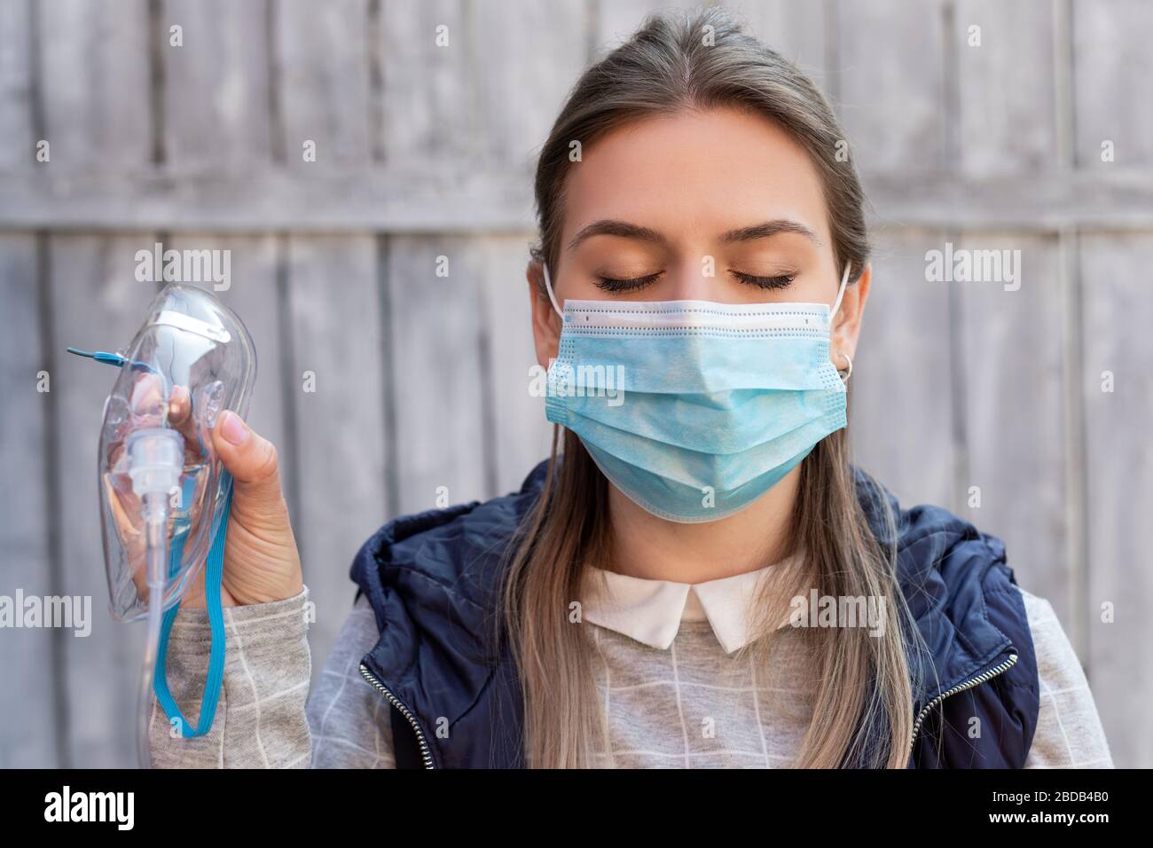 Woman wearing surgical mask is holding a medical oxygen mask outside