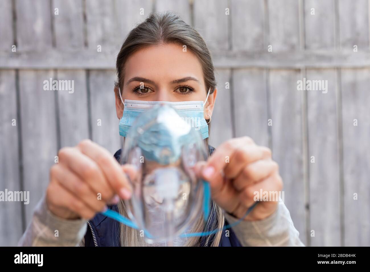 Woman wearing surgical mask is holding a medical oxygen mask outside