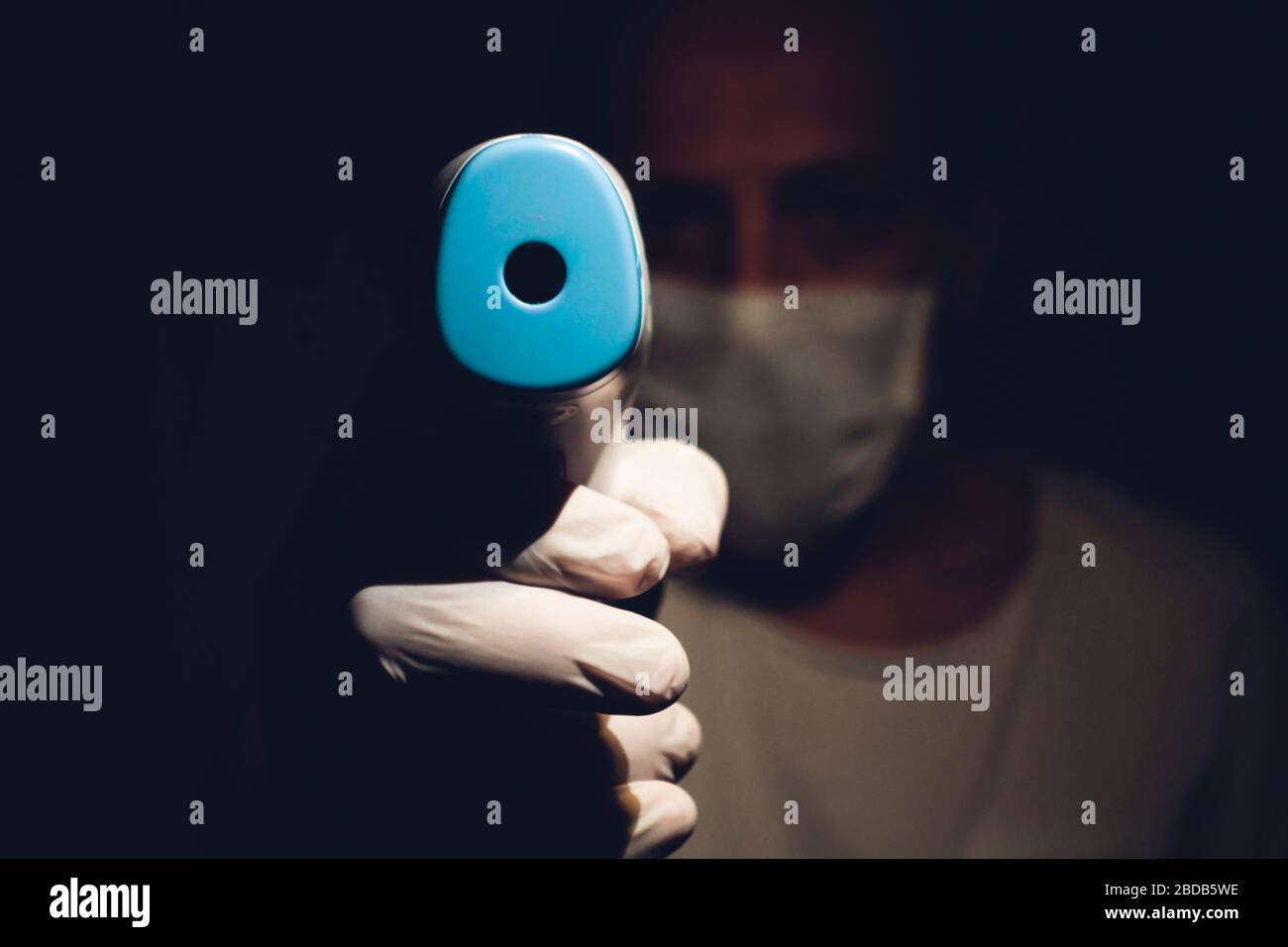 Male Health Worker Points Out a Infrared Thermometer to the camera Point of View- Dark Scary Stock Photo