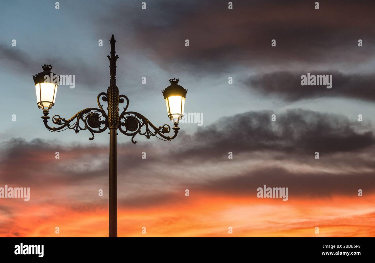 Looking up at an Illuminated decorative cast iron streetlight in front of a colourful sunset Stock Photo