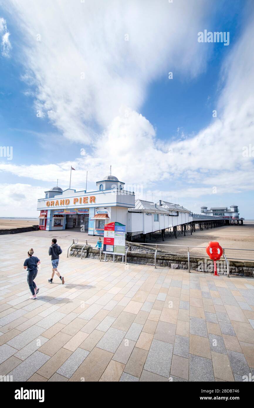 A couple of joggers pass the Grand Pier while taking their allowed daily exercise at Weston-super-Mare during the Coronavirus lockdown UK Stock Photo