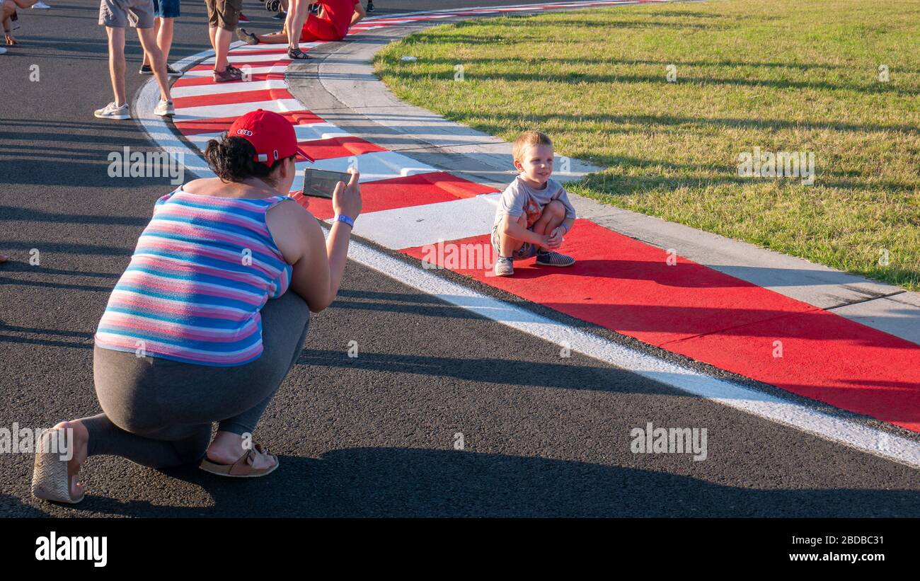 Mogyorod Hungary 08 01 2019: Mother photographs her son on the red and white sidewalks of the Motor Speedway. Stock Photo