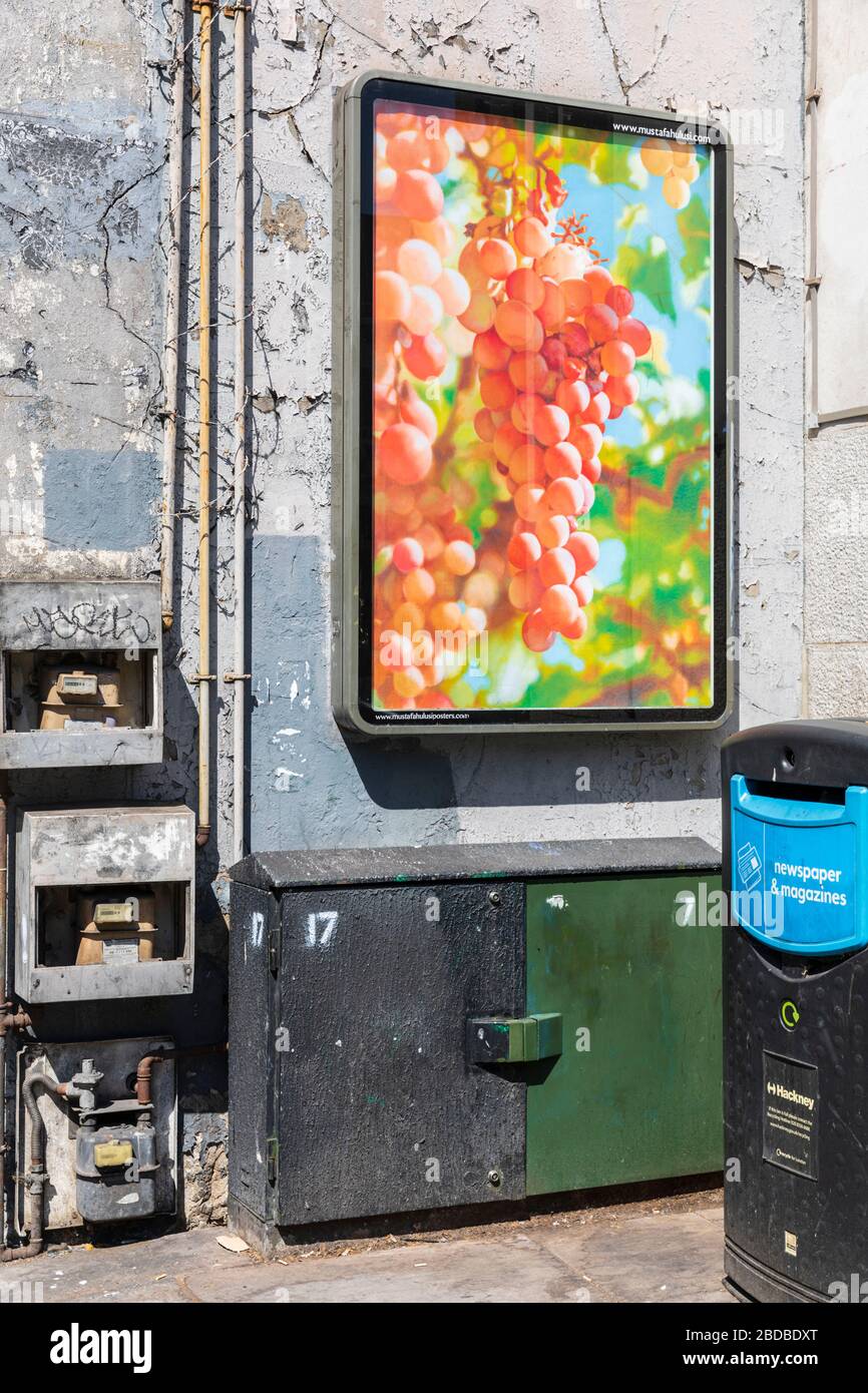 An advertisement screen displays lush and juicy ripe pink grapes in a dirty and decayed corner of Shoreditch in London, UK. Stock Photo