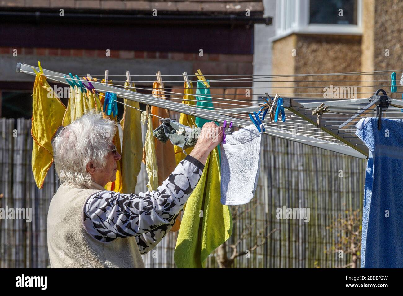 Older lady hanging out dusters on a rotory cloths line  having just been wash in a backgarden, Northampton, England, UK. Stock Photo