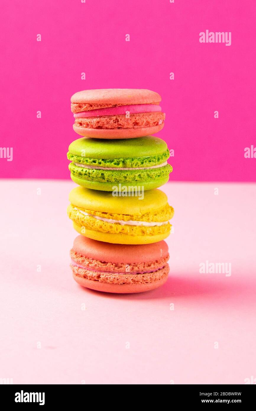 Multi-colored macaroons stand in a pile on a pink table Stock Photo
