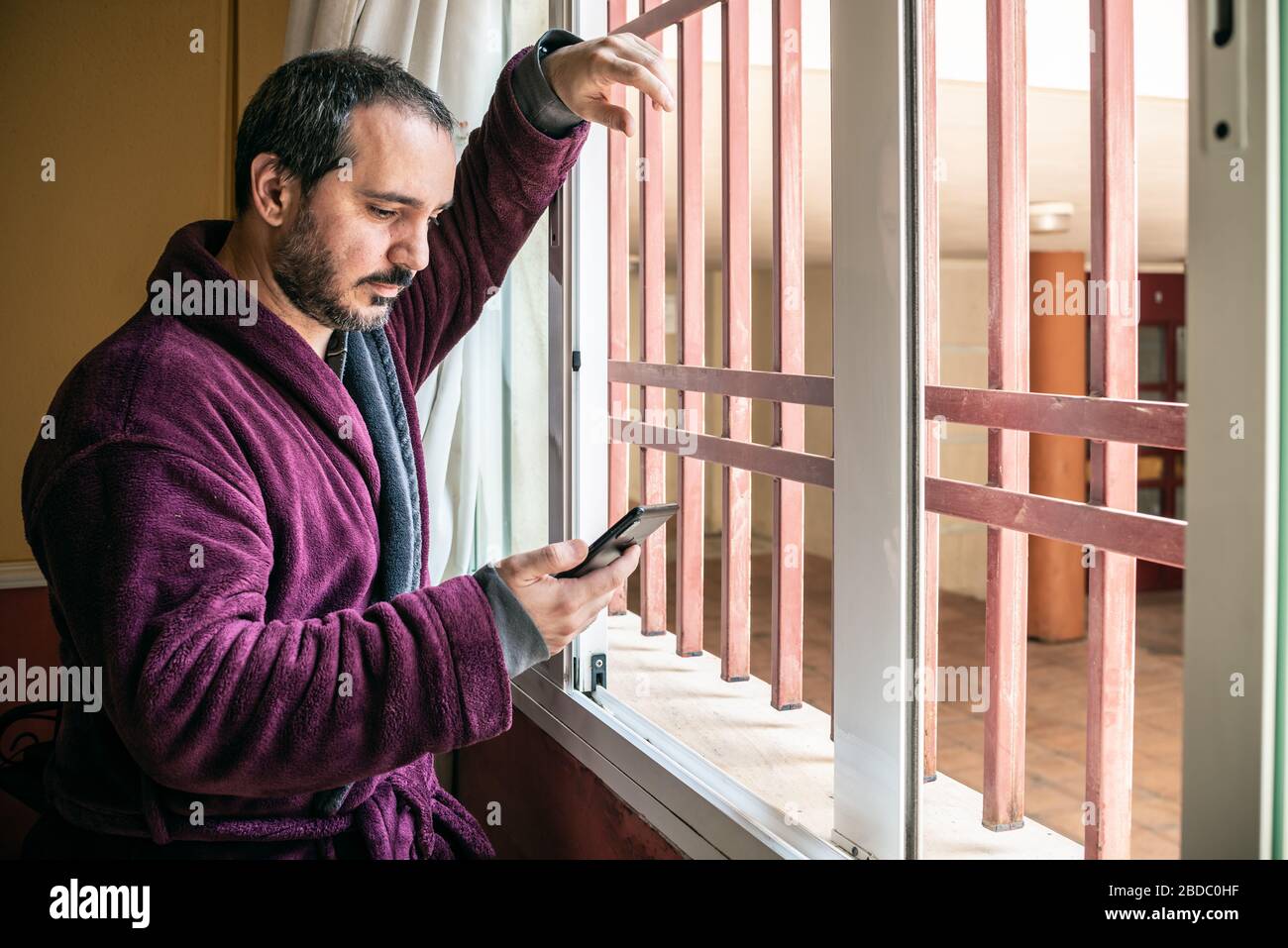 man looking through the window and using the smartphone Stock Photo