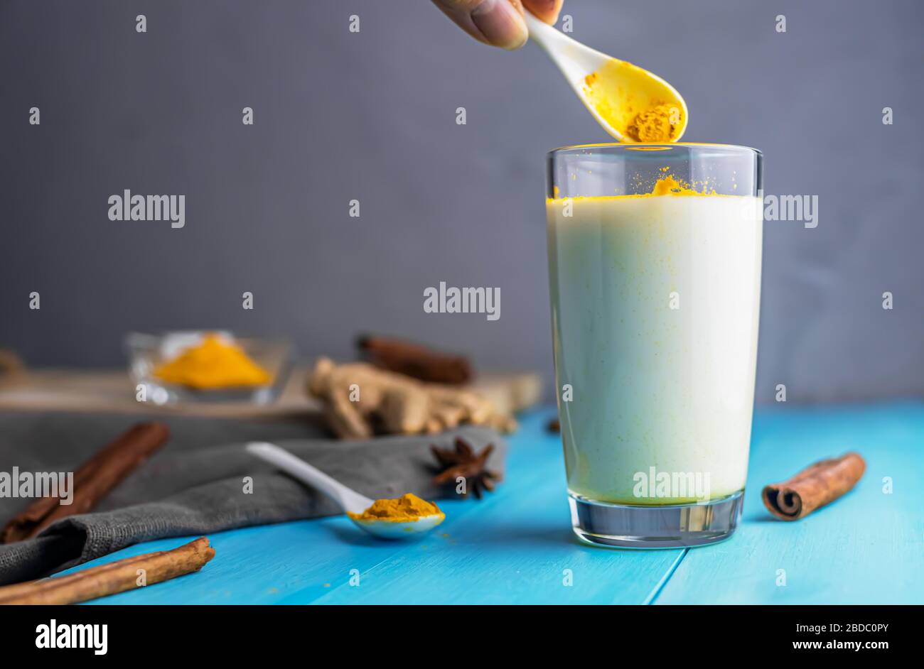 turmeric is poured into milk for golden milk, milk with turmeric, spices. with a drinking tube. on a blue wooden background. with copy space Stock Photo