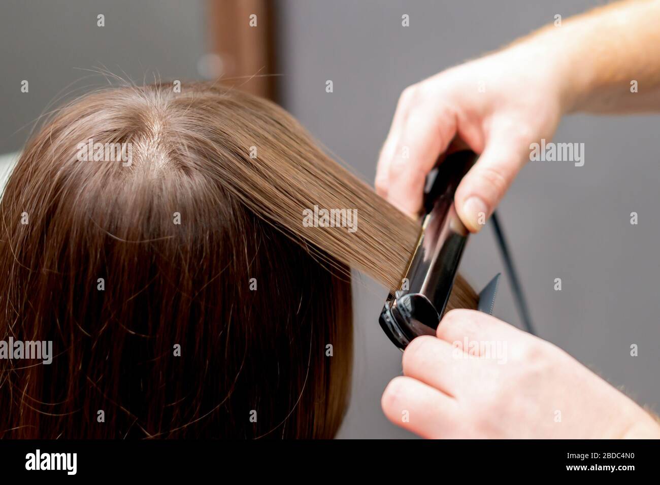 Hairdresser straightens hair of woman with hair straightener tool in hair  salon Stock Photo - Alamy