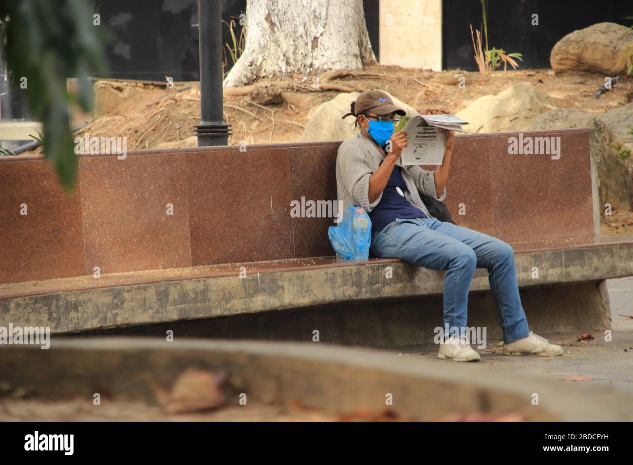 Caracas, Venezuela March 31, 2020: A woman wearing mask reads the newspaper in public park ignoring the stay at home order amid spread of covid-19 Stock Photo