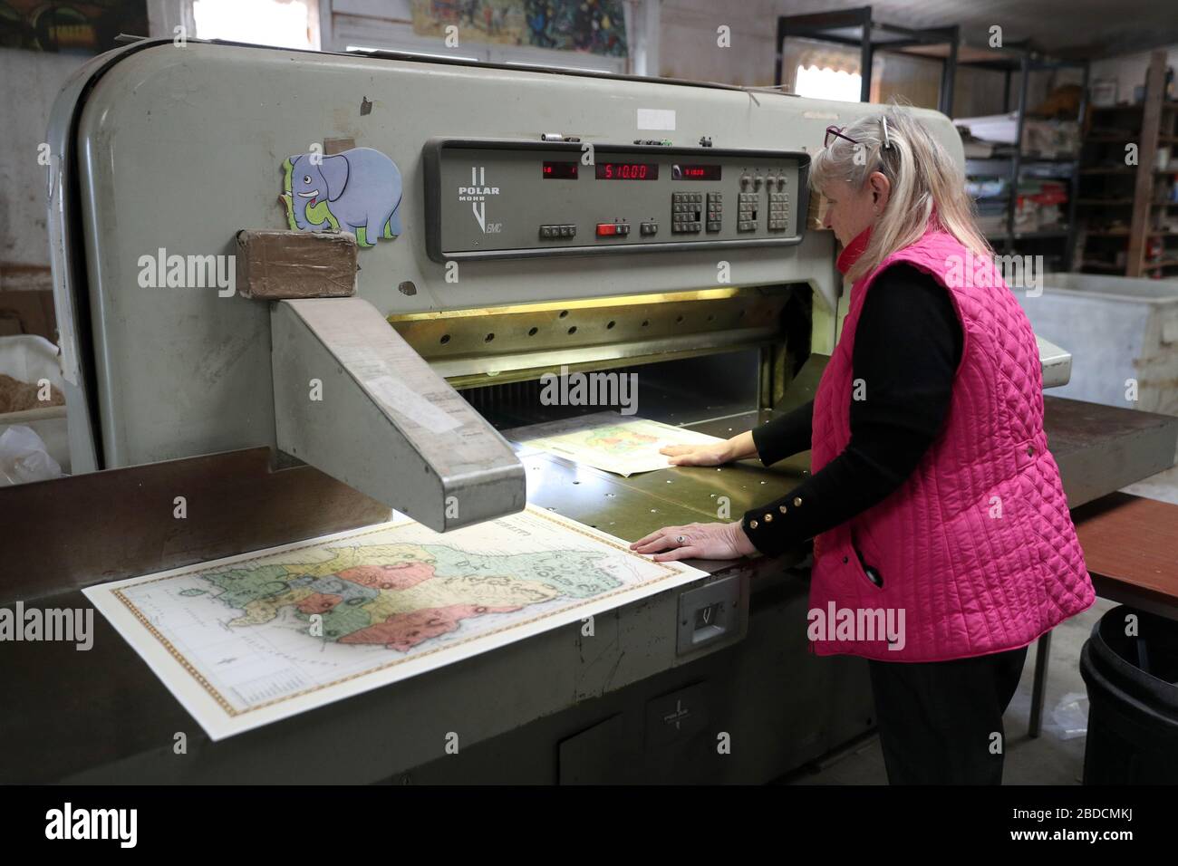 Julie Wilkins uses a guillotine to trim the edges of a print for a