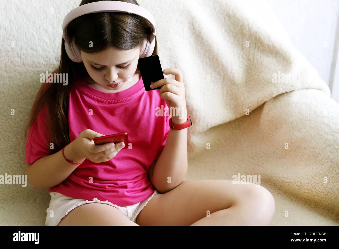 Cheerful girl in pink headphones sits with a phone in her hand and a credit card Stock Photo