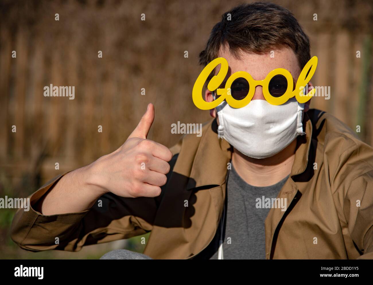 Portrait of a young man in a mask and funny sunglasses, indicating with gestures that everything will be fine.  Stock Photo
