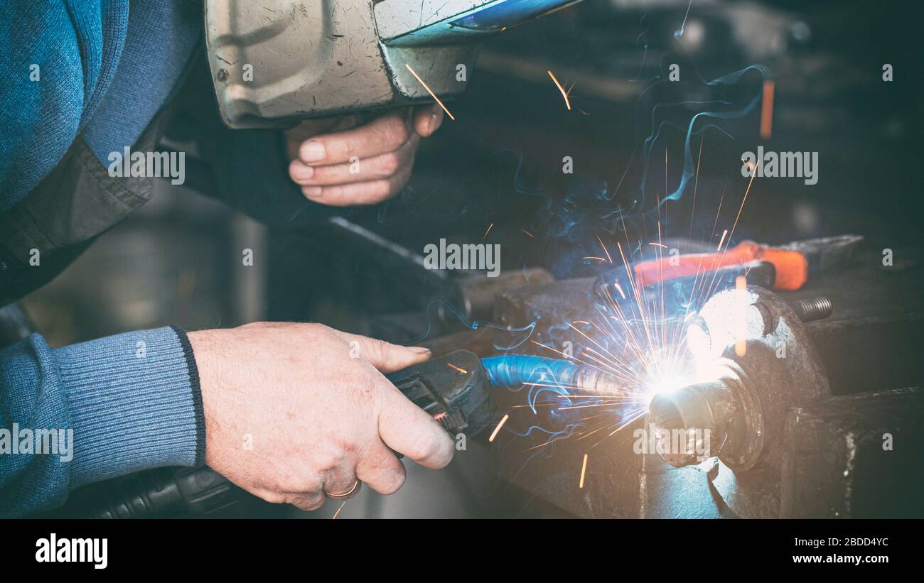 Locksmith welder welds a workpiece in a workshop. Stock Photo