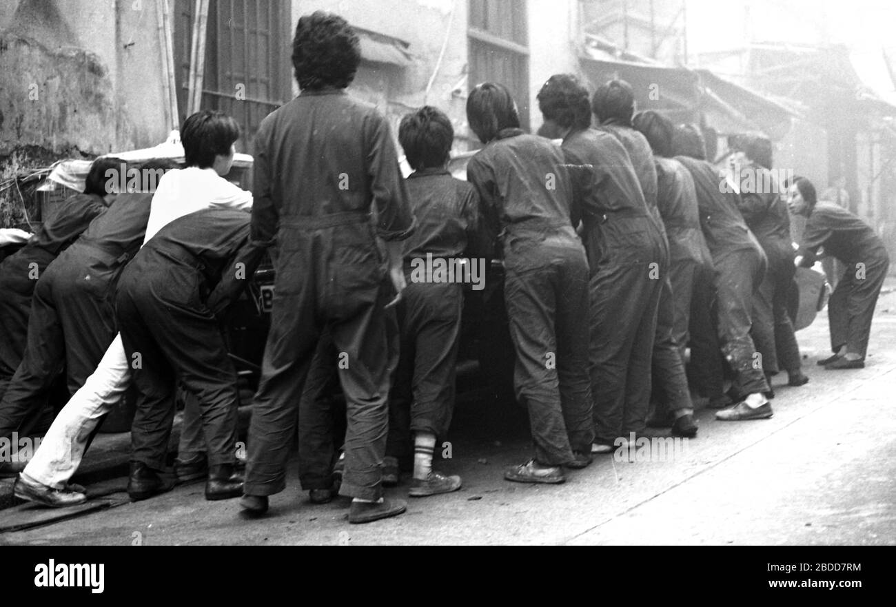 Emergency services including fire crews attend a building fire in Kennedy Street, of Queen's Road East on Hong Kong Island in 1979 as a team of workers in overalls try to bump a car to safety. Photo by Tony Henshaw Stock Photo