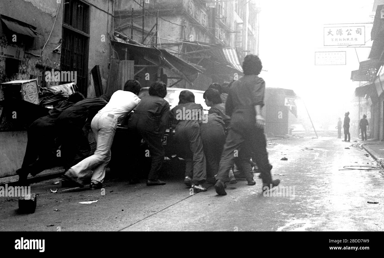 Emergency services including fire crews attend a building fire in Kennedy Street, of Queen's Road East on Hong Kong Island in 1979 as a team of workers in overalls try to bump a car to safety. Photo by Tony Henshaw Stock Photo