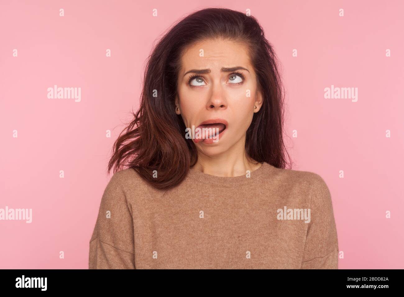Portrait of funny silly young woman with brunette hair looking cross eyed and sticking tongue out, making dumb brainless face, disobedient goofy expre Stock Photo