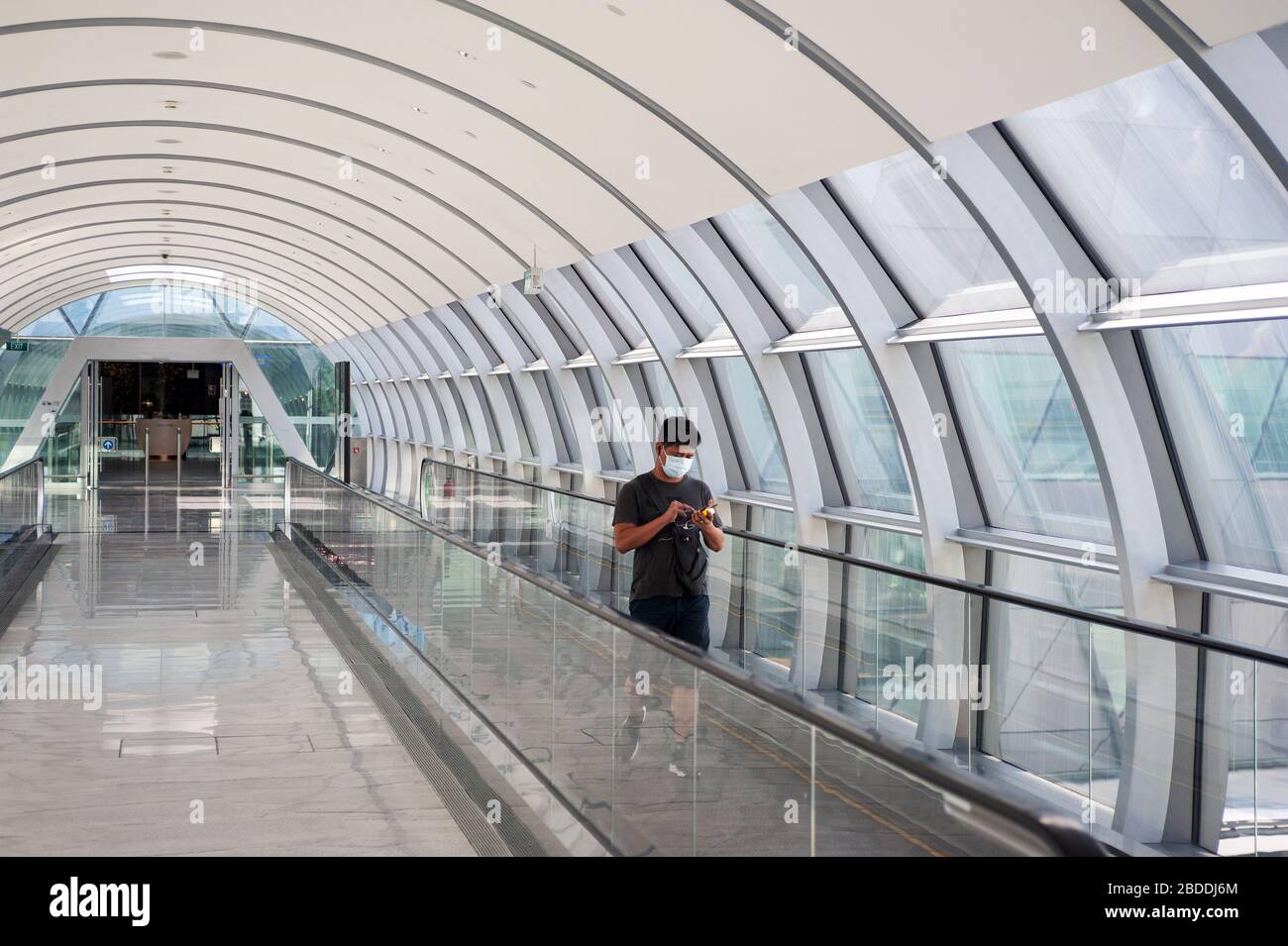28.03.2020, Singapore, , Singapore - A man is walking along the connecting bridge between Jewel Terminal and Terminal 2 at Changi Airport, wearing a r Stock Photo