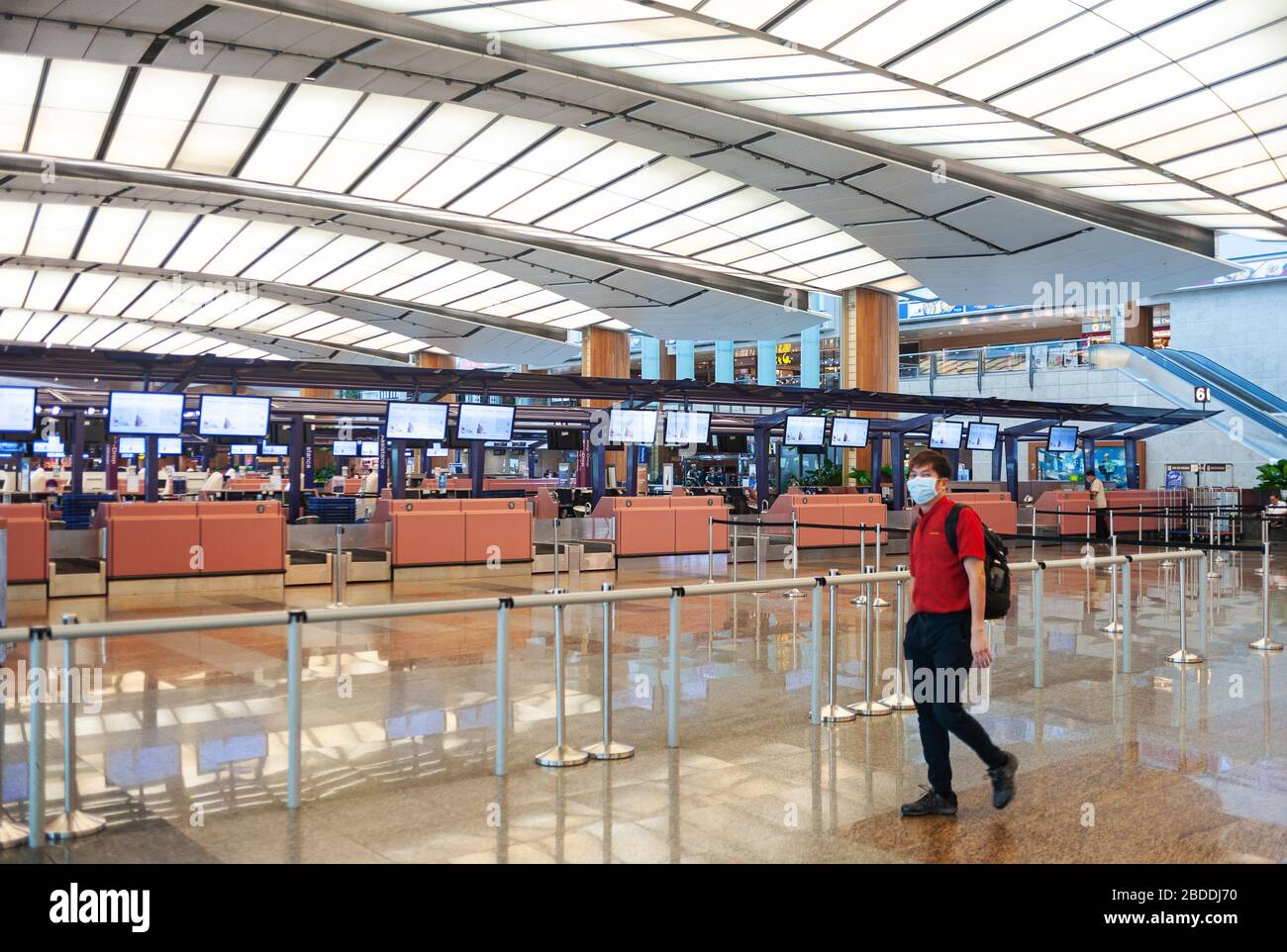 28.03.2020, Singapore, , Singapore - A man walks past closed departure counters in the empty departure hall of Terminal 2 at Changi Airport, wearing a Stock Photo