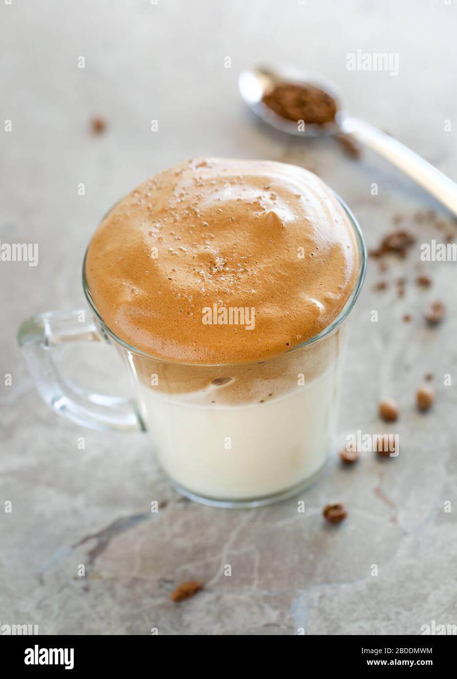 Dalgona Coffee Cream with milk in glass cup with spoon in the background Stock Photo
