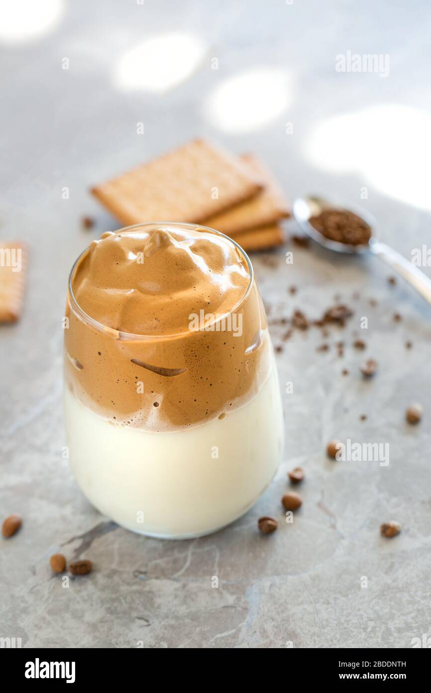 Dalgona Coffee Cream with milk in glass cup with spoon in the background Stock Photo