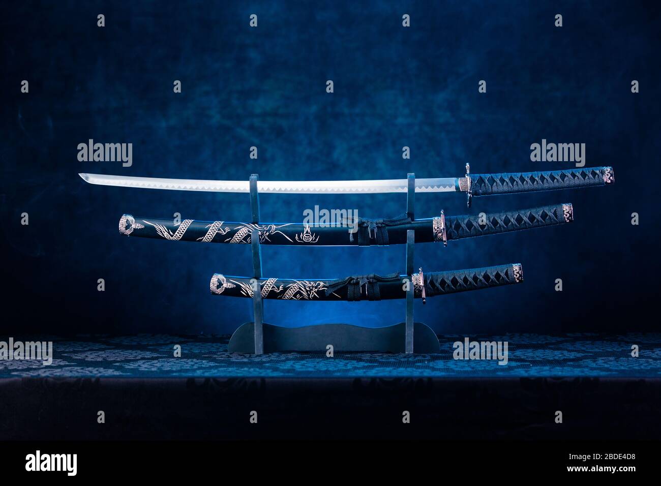 Three swords on stand, katana blade exposed, blue light behind Stock Photo