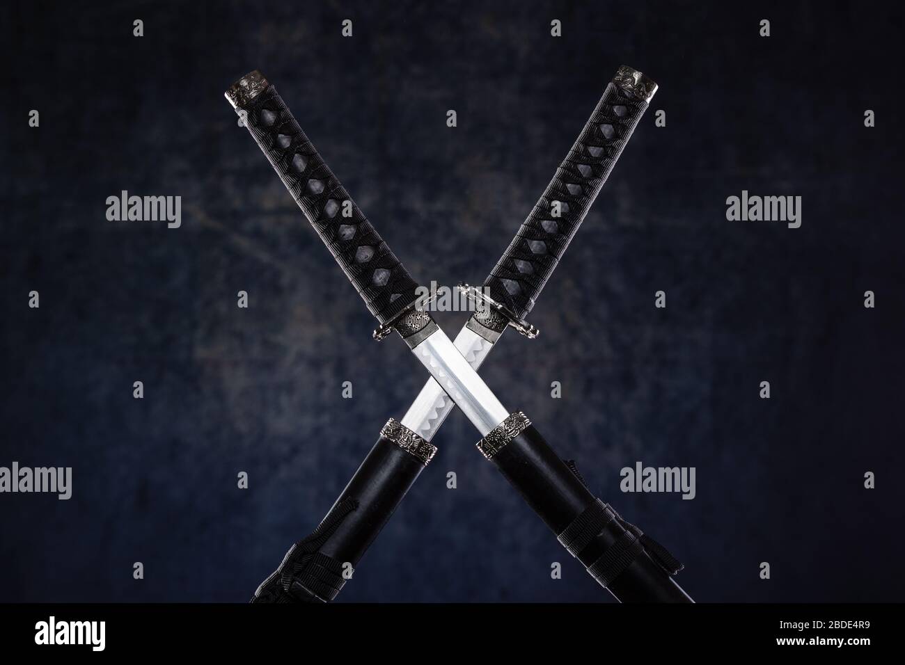 Two crossed katanas with partially drawn blades on dark background Stock Photo