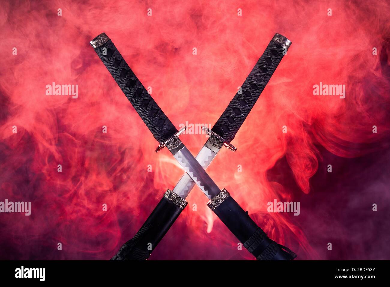 Partially drawn blades of two katanas in red smoke Stock Photo