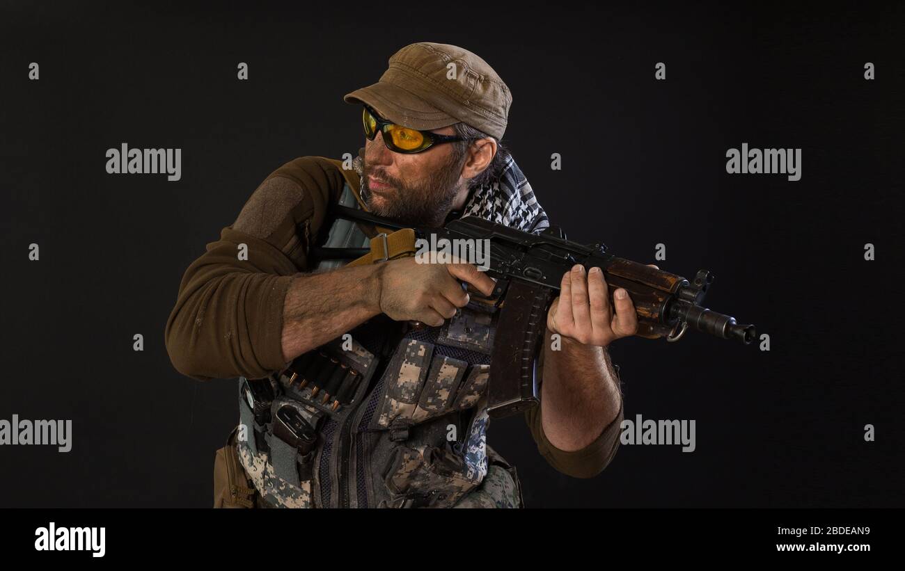 Soldier mercenary with a gun looking by side. Photo on a dark background. Modern private army concept. Stock Photo