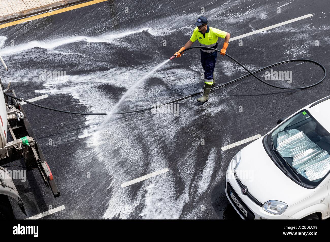 Council worker hosing down the streets with a disinfectant wash during the coronavirus lockdown, Playa San Juan, Tenerife, Canary Islands, Spain Stock Photo