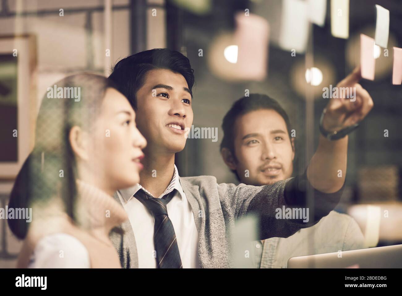 three asian small company businesspeople young entrepreneurs meeing discussing in office using sticky notes Stock Photo