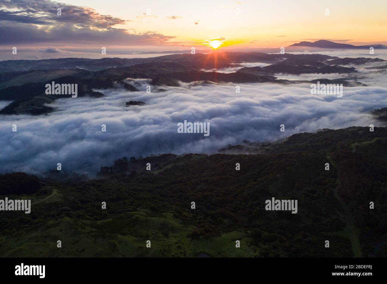 A beautiful sunrise illuminates fog as it rolls through valleys in Northern California. Just west of these hills and valleys is San Francisco Bay. Stock Photo