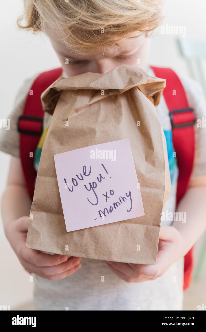 Boy (4-5) peeking into lunch bag with note from mom Stock Photo