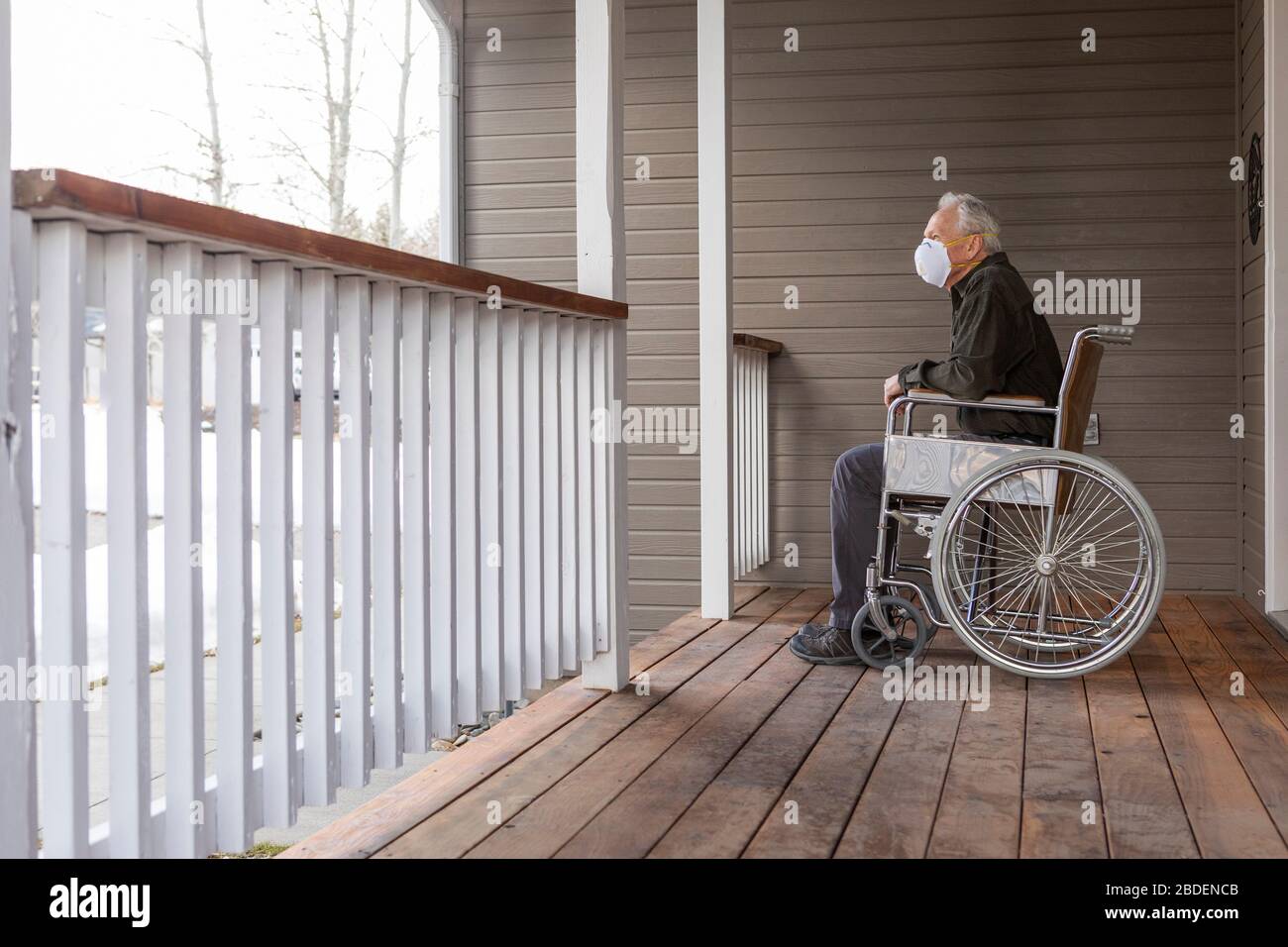 Senior man in wheelchair wearing protective mask to prevent coronavirus transmission on porch Stock Photo