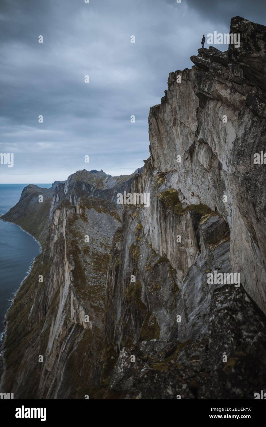 Norway, Senja, Man standing on the edge of steep cliff on top of Segla mountain Stock Photo