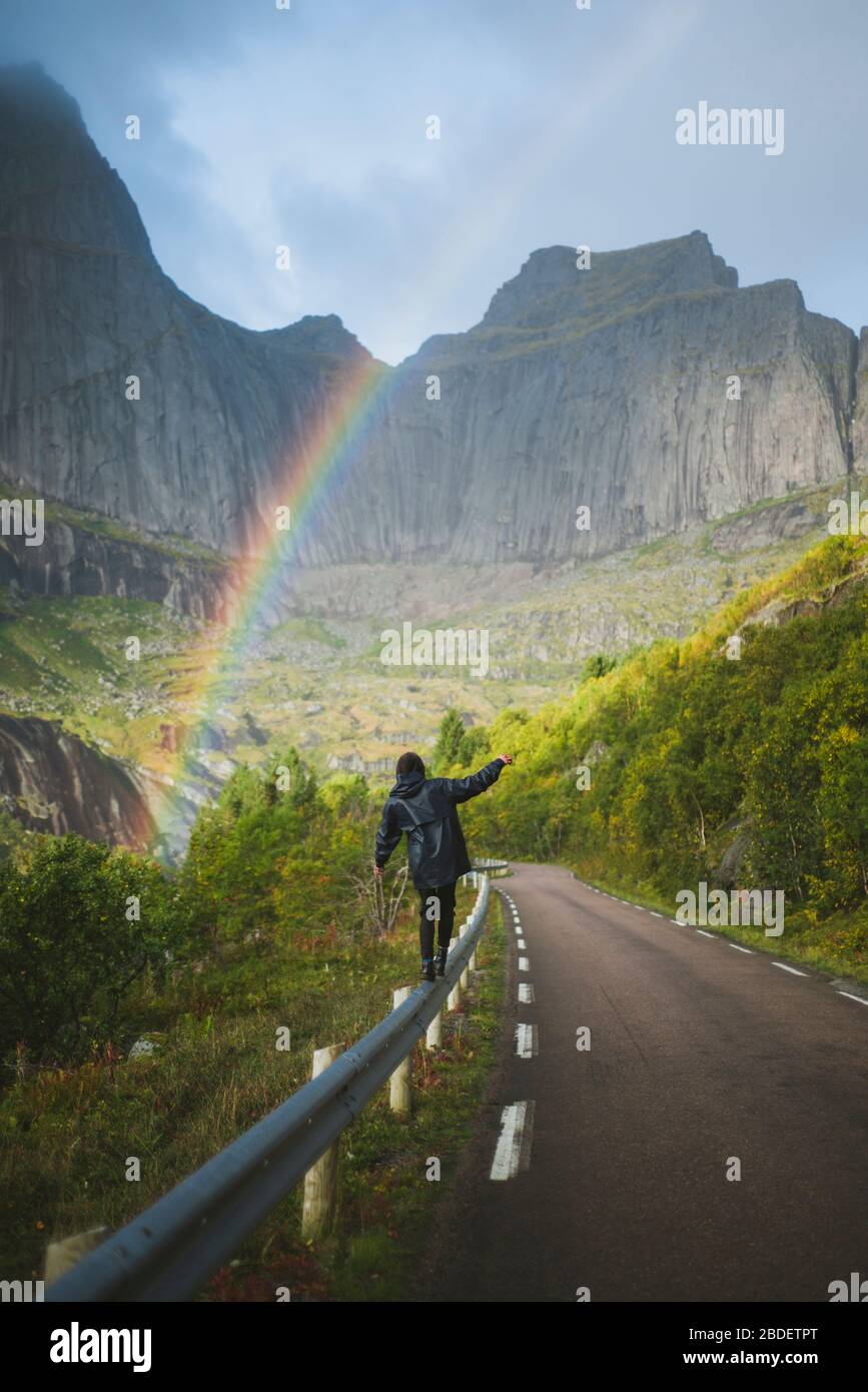 Norway, Lofoten Islands, Man balancing on crash barrier with mountains and rainbow in background Stock Photo