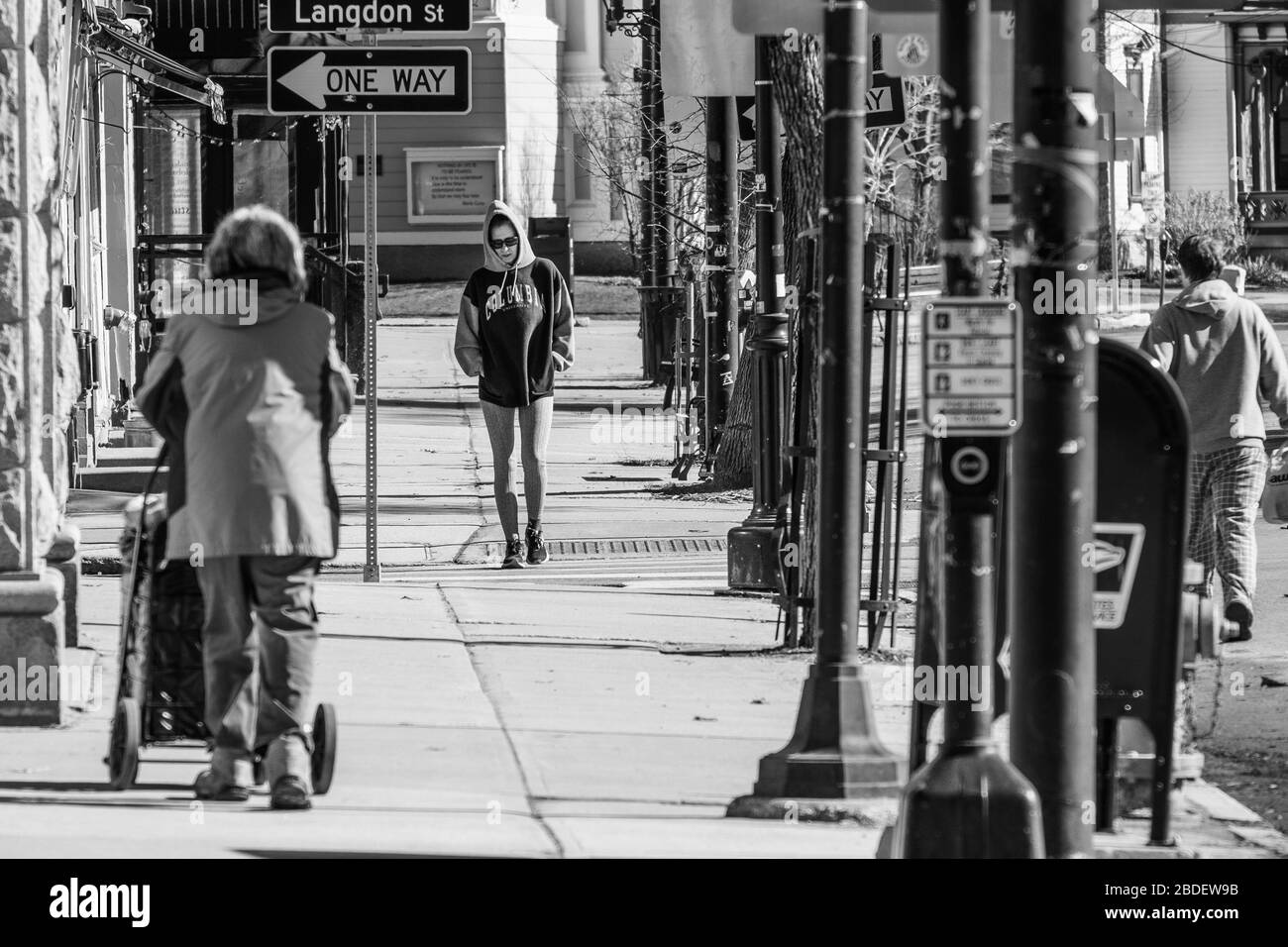 Three pedestrians carefully keep their distance in downtown Montpelier, VT, USA, capital of Vermont, during social distancing and stay-at-home order. Stock Photo