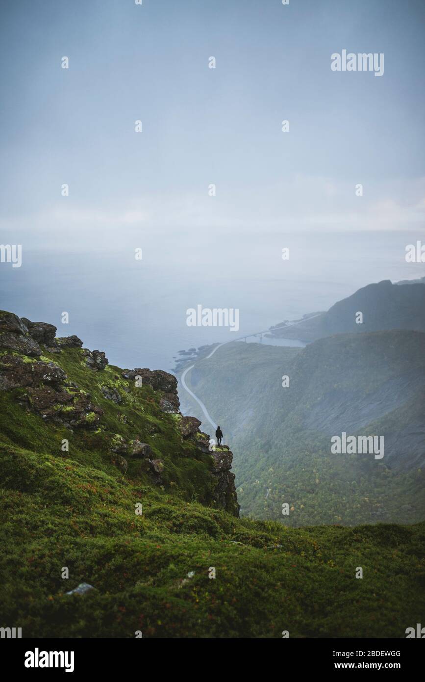 Norway, Lofoten Islands, Reine, Man looking at view fromÂ ReinebringenÂ mountain during rain Stock Photo