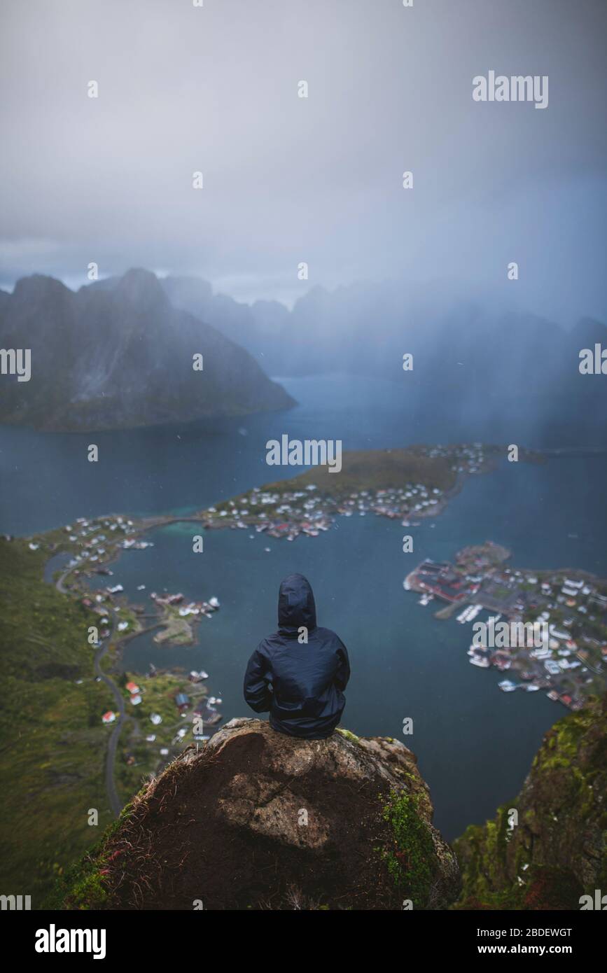 Norway, Lofoten Islands, Reine, Man looking at fjord from Reinebringen mountain during rain Stock Photo
