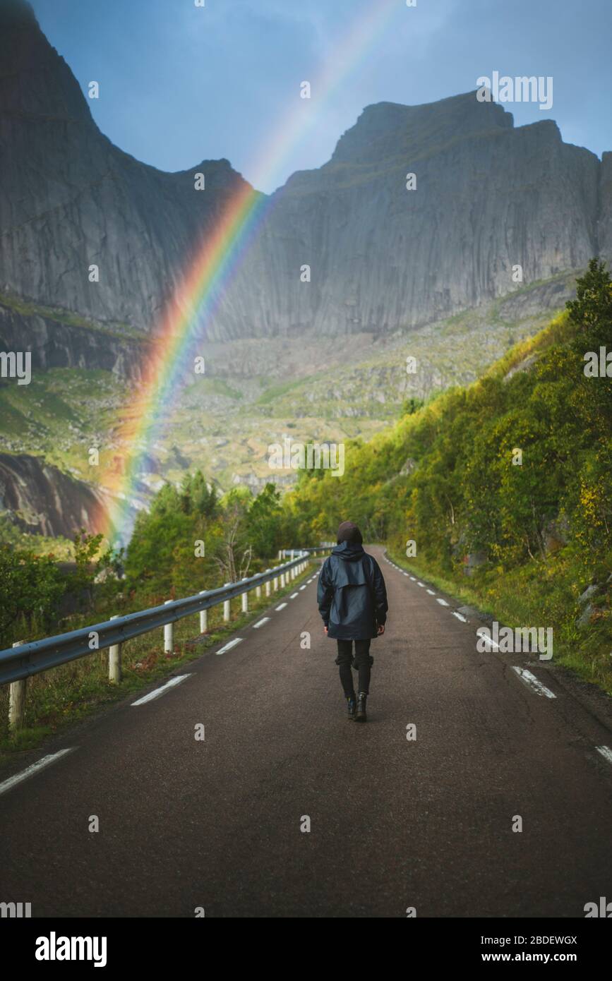 Norway, Lofoten Islands, Man walking down road with mountains and rainbow in background Stock Photo
