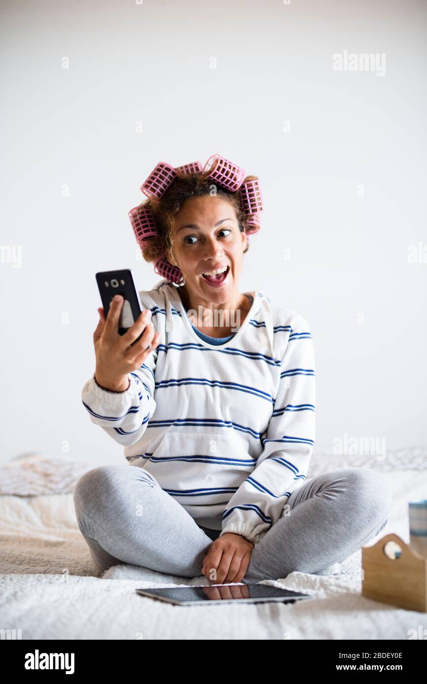 Woman with hairÂ curlersÂ sitting on bed and taking selfie Stock Photo