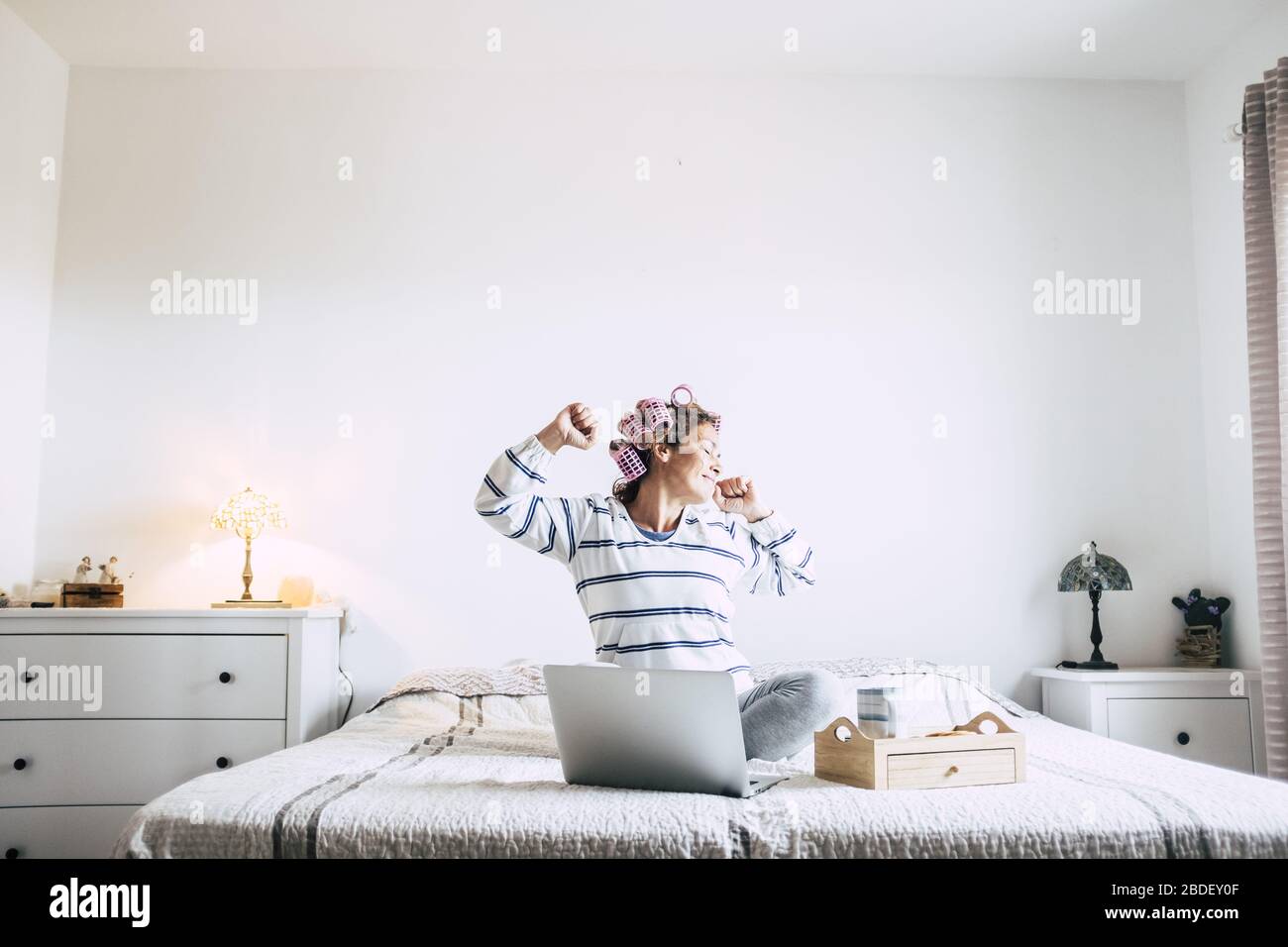 Woman sitting on bed with laptop and stretching Stock Photo