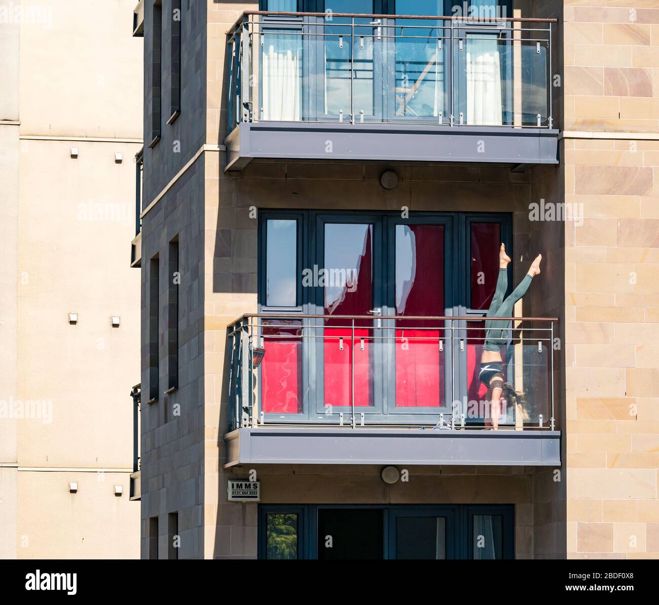 Leith, Edinburgh, Scotland, UK. 8th Apr, 2020. Covid-19 lockdown: on one of the warmest sunny days so far this year with people in lockdown. A woman practices acrobatic handstands on a balcony in the sunshine Stock Photo