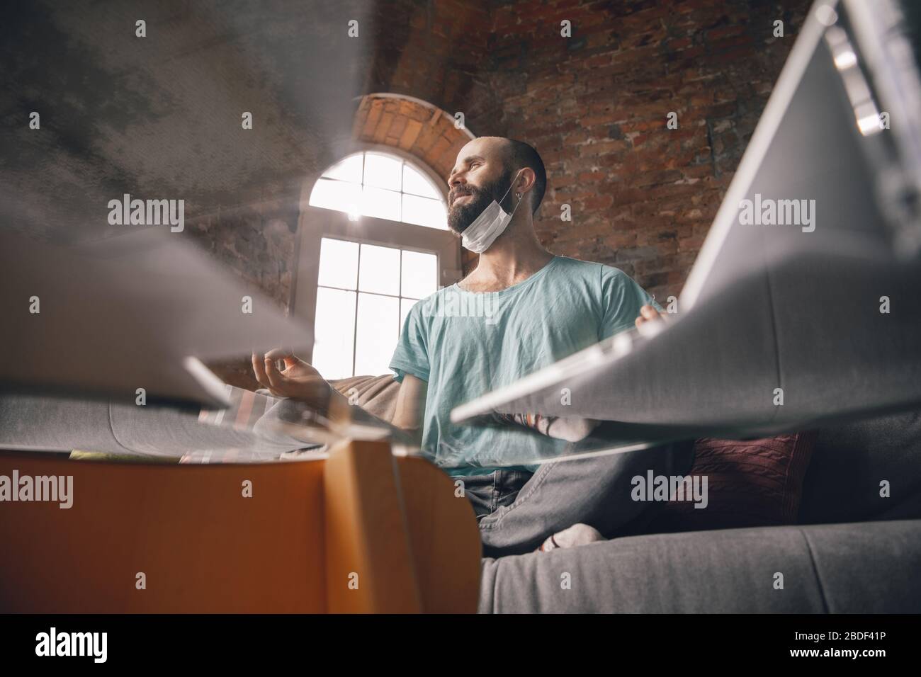 Paperwork. Young man doing yoga at home while being quarantine and freelance online working. Remote office, isolated. Concept of healthy lifestyle, wellness, being safe while coronavirus pandemic. Stock Photo
