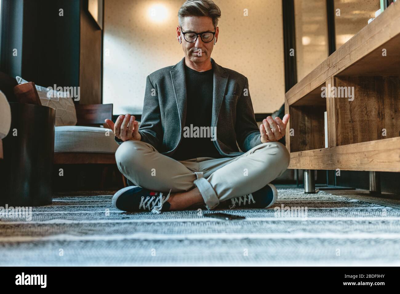 Businessman sitting on floor and meditating in yoga pose. Mature businessman doing relaxation yoga in office lounge. Stock Photo